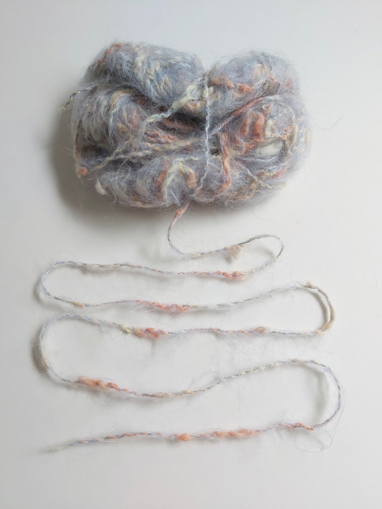 A ball of pale grey knitting yarn with slubs in shades of grey and peach.