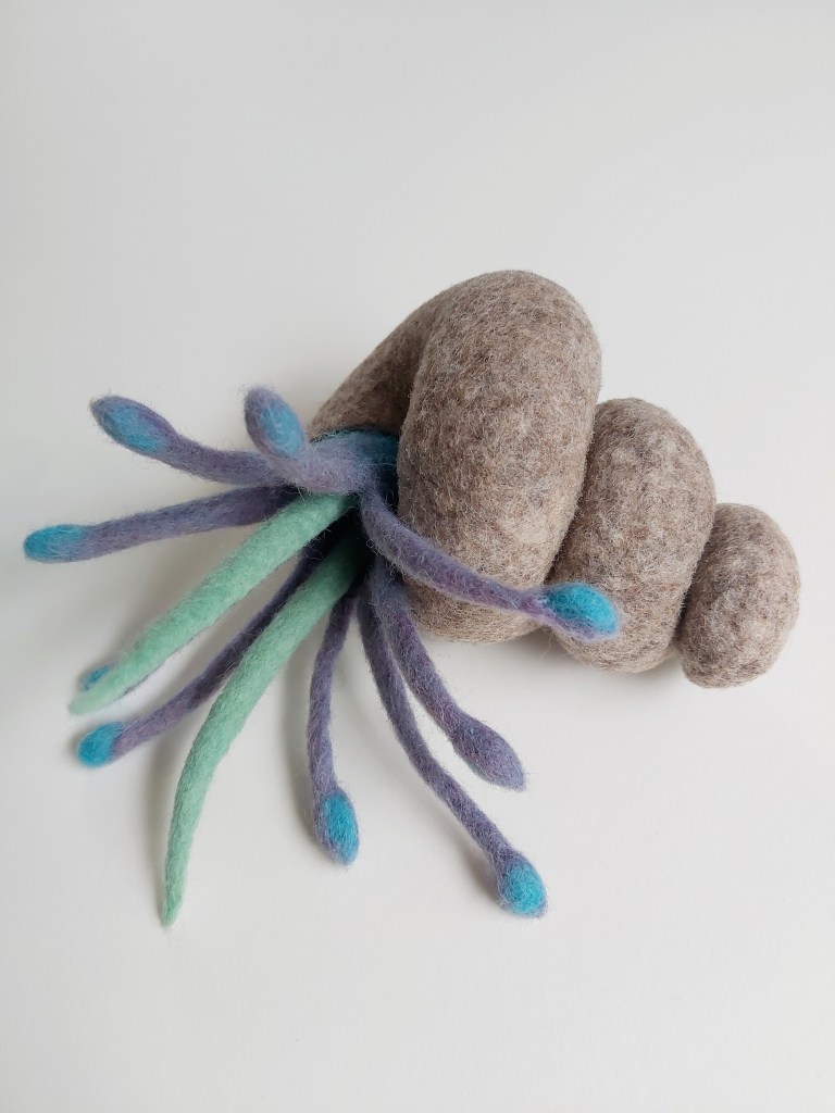Photo of a beige coloured Wet felted spiral shell with abstract hermit crab poking out of it.
